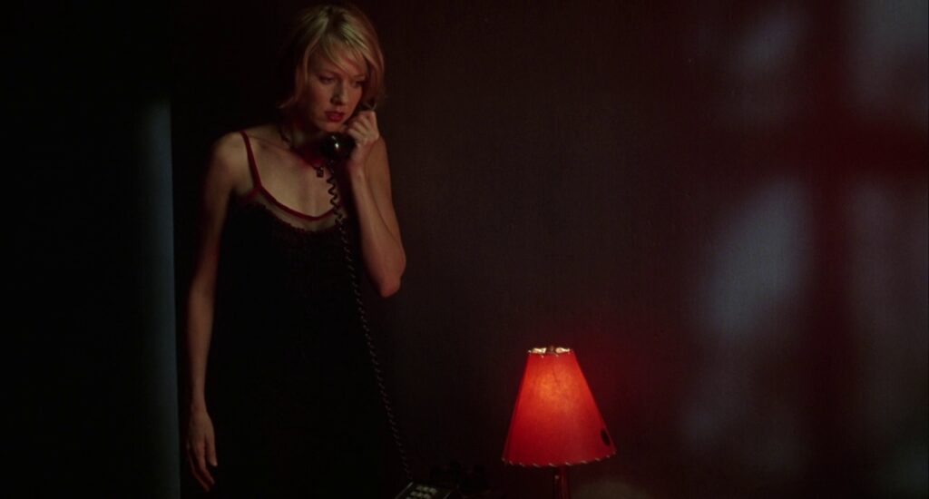 Actress Naomi Watts in David Lynch's film Mulholland Drive. She gribs a telephone and looks with a concerned expression, lit in the glow of a small red lamp in the evening.